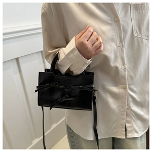 Detail of black PU leather handbag with decorative bows and geometric top cut design