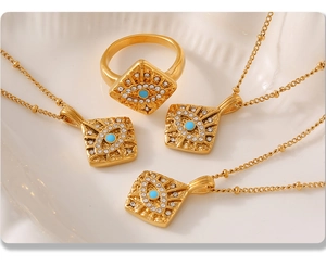 Detailed view of Evil Eye square charms on gold necklaces and ring on a ceramic tray
