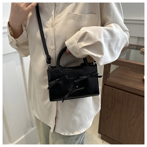 Fashionable black leather handbag with chic bow details shown on model for size reference