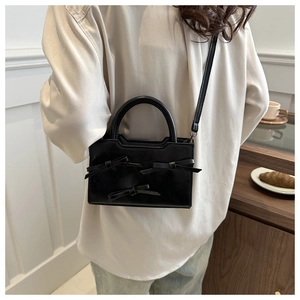 Détail d'un sac bandoulière noir avec trois nœuds décoratifs et une poignée supérieure