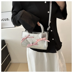 Détail du sac à main argenté avec trois nœuds roses et une bandoulière amovible