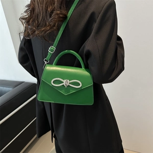 Felgroene crossbodytas met strass-strik gedragen door model in een strak zwart pak