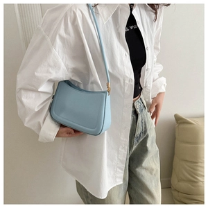 Sky blue minimalist half-moon crossbody bag with golden hardware shown on shoulder
