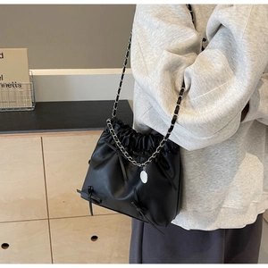 Close-up of black PU drawstring bucket bag with silver chain strap and bow detail