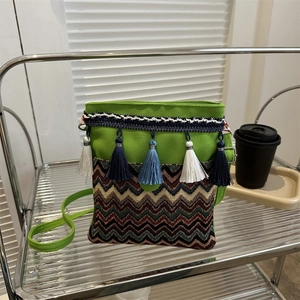 Detail of green canvas crossbody bag featuring colorful woven waves and tassel accents