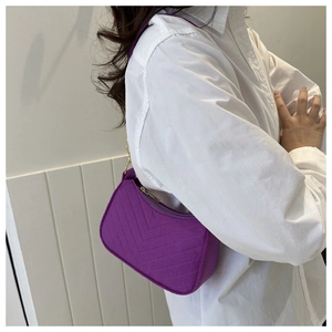 Detail of purple V-quilted crescent shoulder bag with golden zipper on white shirt