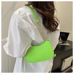 Detail of neon green quilted baguette bag with gold chain strap on model's shoulder