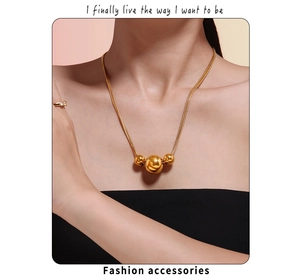 Close-up of three gold geometric sphere beads on a minimalist necklace worn by a model