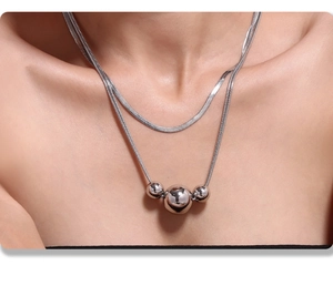 Macro shot of double-layered silver necklace with flat blade chain and three shiny beads