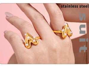 Detail of gold heart lava rings with pearls on model hand over pink background