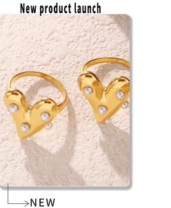Detailed view of two gold heart-shaped rings with white faux pearls on stone background