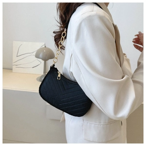 Detail of black quilted shoulder bag with gold chain strap on white blazer