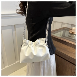 Close-up of a white pleated bucket bag with a silver chain strap worn by a model