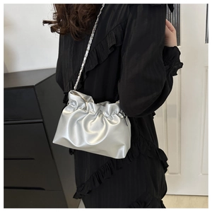 Detail of silver pleated bucket bag with metallic chain strap worn on the shoulder