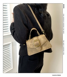 Detail of khaki suede satchel featuring a textured golden square buckle and top handle