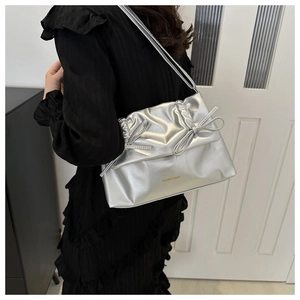 Silver metallic shoulder bag with bow details and pleats shown on a model