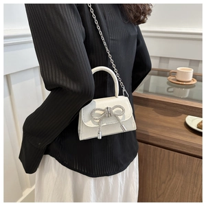 Close-up of white mini handbag with sparkling rhinestone bow and silver chain strap