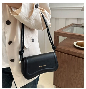 Detail of black leather underarm bag with gold logo and decorative knot strap detail