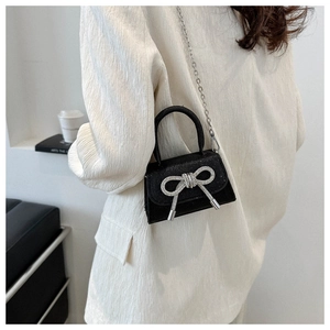 Close-up of a mini black crossbody bag with a silver rhinestone bow on a stylish model
