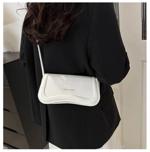 Detail of a white leather crossbody bag with Miss mini logo on a black blazer outfit