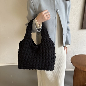 Fashionable black bubble textured tote bag with pleated design worn by a model in a minimal room