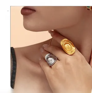 Close-up of exaggerated gold and silver oval hat-shaped rings worn on a hand