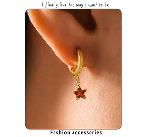 Macro view of gold hoop earring with a red star glass pendant worn by a model