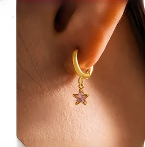Close-up of model wearing gold hoop earrings with a dangling pink star zircon pendant