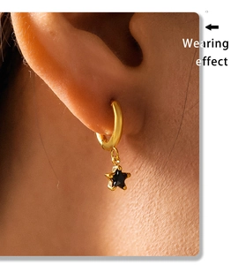 Detailed close-up of 18K gold plated star dangle earrings worn on a person's ear lobe