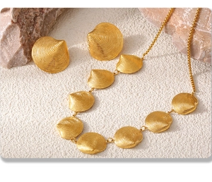 Detailaufnahme des goldenen Muschel-Schmucksets aus Kette und Ohrringen auf weißem Sand