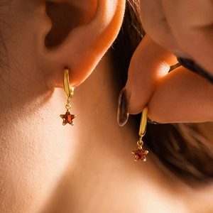 Elegant gold star drop earrings with sparkling red zircon crystals on female model