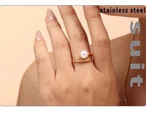 Macro detail of open gold steel ring featuring a white pearl and paved zircons on finger