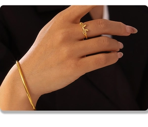Dettaglio dell'anello a fiocco e bracciale rigido dorato 18K indossati sul polso della modella