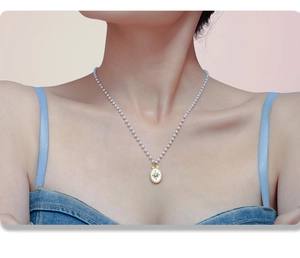 Dettaglio di collana con perle e ciondolo ovale dorato a stella indossato da modella