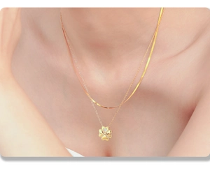 Detalle de collar dorado de doble capa con colgante de trébol y grabado de maman