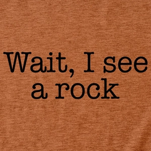 Detail of black text Wait I see a rock print on warm brown cotton T-shirt fabric