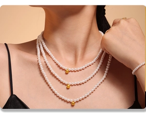 Close-up of layered baroque pearl necklace set with golden sphere pendants on a model