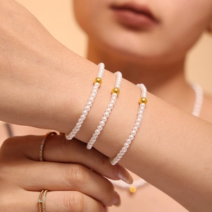 Elegant triple-layered white pearl bracelet with gold beads worn on a model's wrist