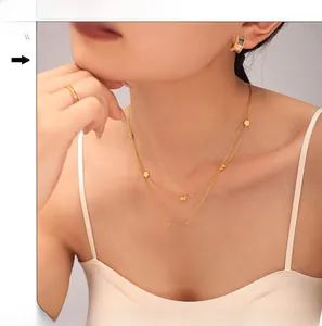 Detail of a double-layer gold necklace with infinity symbol and clover accents on model