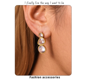 Detail of three-stone drop earrings in 18K gold plated steel on a model's ear