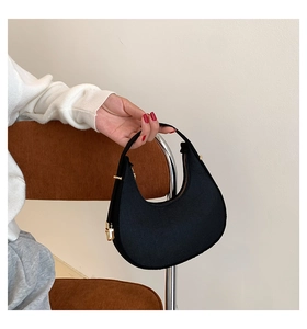 Detail of black suede crescent bag with gold zipper held by hand against a retro chair