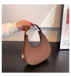 Detail of crocodile embossed brown crescent bag with gold hardware and hand strap