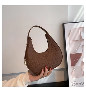 Detail of crocodile-embossed brown crescent bag with gold zipper and stylish handle