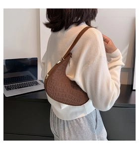 Detail showing deep brown crocodile pattern texture and gold buckle on crescent shoulder bag
