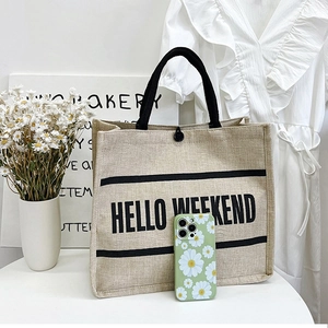Detail of beige linen tote bag featuring Hello Weekend print and black braided handles