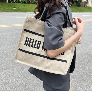 Detail of a large jute tote bag with black handles and Hello World printed text