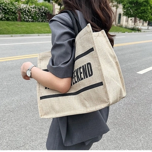 Close-up of the textured linen tote bag featuring a bold black WEEKEND print and handles