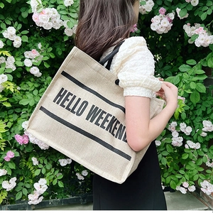 Outdoor shot of large linen tote bag with HELLO WEEKEND text and black handles