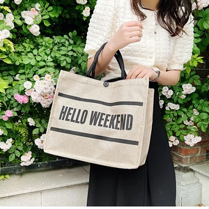 Close-up of beige linen tote bag featuring Hello Weekend print and black braided handles