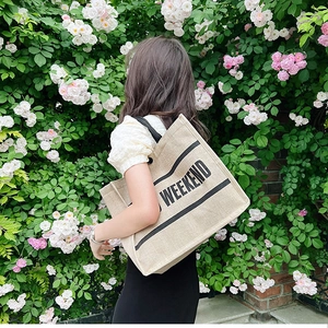 Detailed view of beige canvas tote with black WEEKEND lettering and twin handles